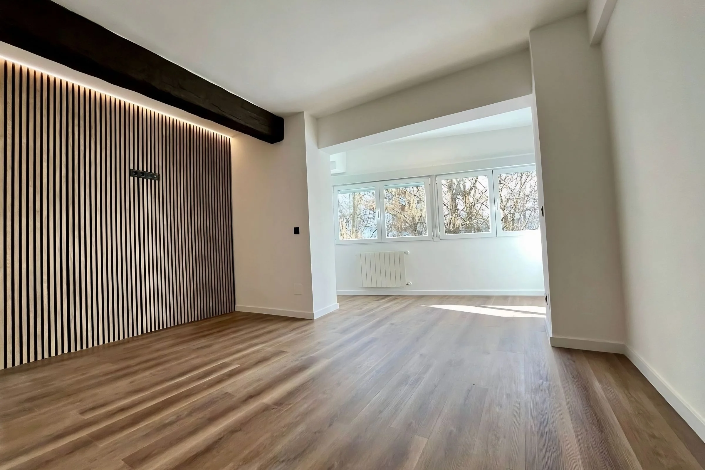 Reforma integral en Alicante — salón con panelado de roble retroiluminado, viga vista original y parquet