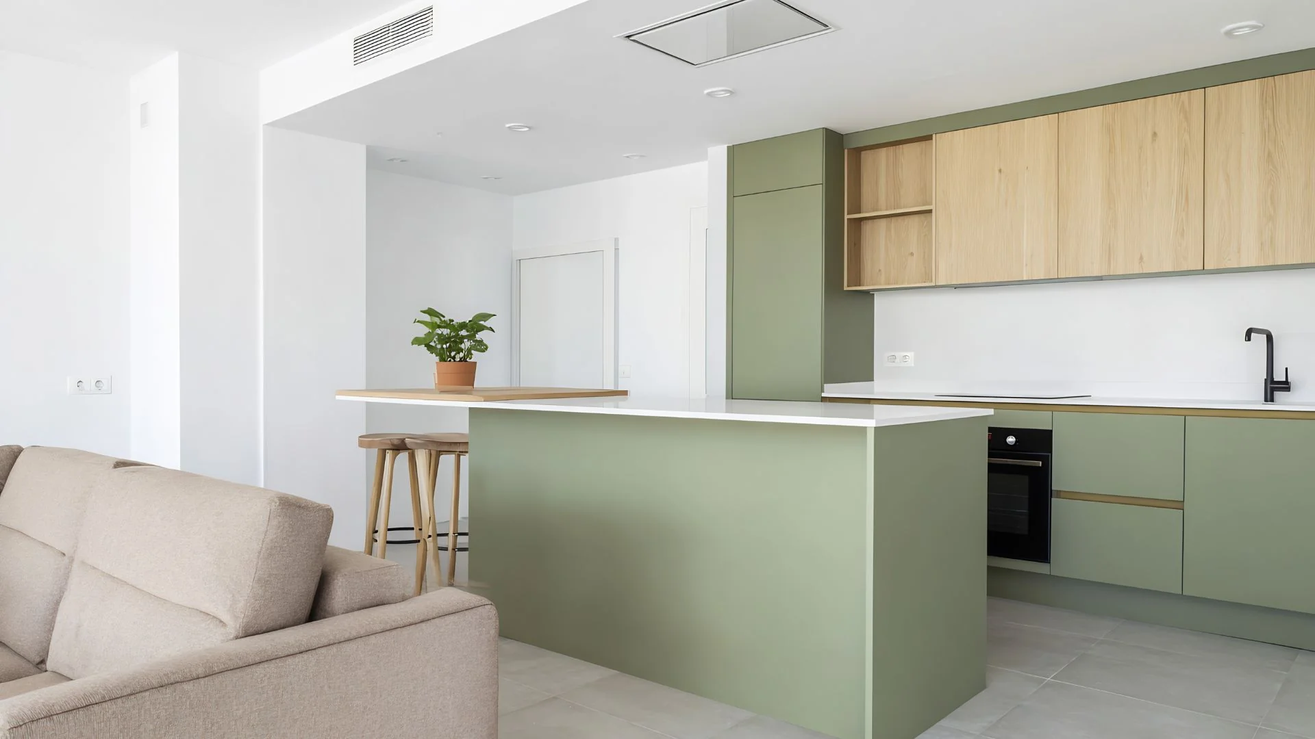 Reforma de cocina abierta al salón en Alicante — isla verde salvia, muebles altos de roble, encimera de cuarzo y grifería negra