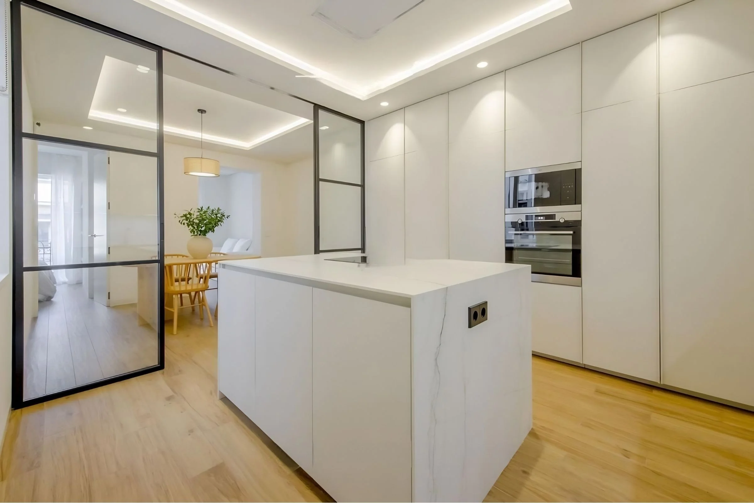 Reforma integral premium en Alicante — cocina isla de mármol con veta, mampara de acero lacado negro y luz perimetral LED
